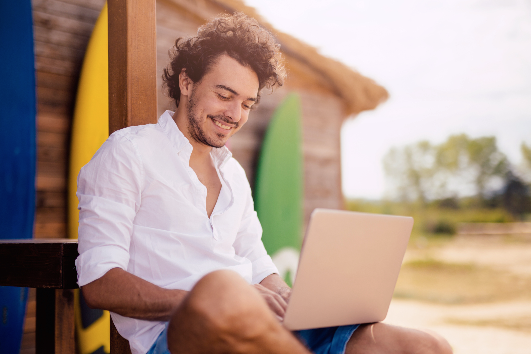 Homem sentado na praia estudando com laptop na perna